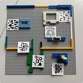 Top-down view of a grey LEGO baseplate with scattered landmark structures and AR marker cards